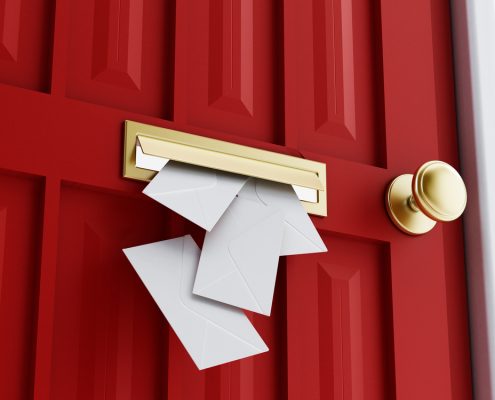 A close up of a red door with a gold colored knob. A mail slot is shown in the center, with several envelopes falling through them.