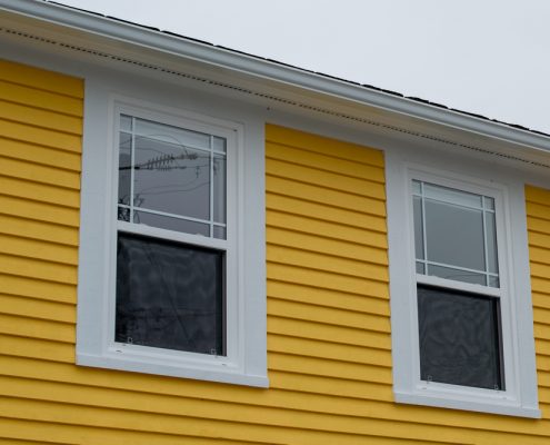 A close up of a yellow home exterior. You can see two double hung windows near the top of the building.