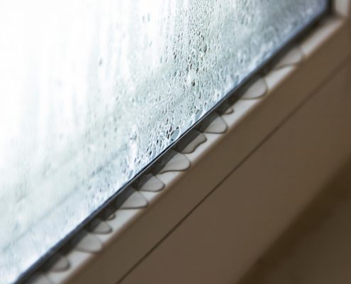 A close up image of the bottom of a window. You can see moisture forming on the window and on the sill holding it, which is a common sign of needing to replace a window.