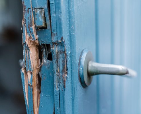 A blue door with chipped and broken wood sticking out of the side.