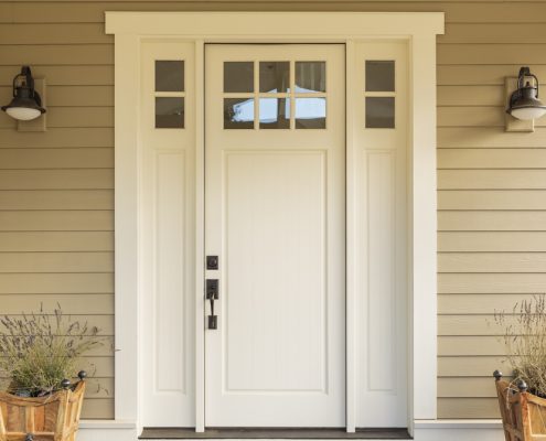 A white entry door with biege tiling surrounding the door. You can see two street lamps and two potted plants on the sides of the door.