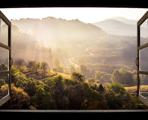 An open window leading to a mountainous, wooded landscape at sunrise.