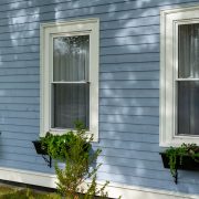 A series of three double hung windows as viewed from the outside of a blue house. You can see a windowsill with plants underneath each window.