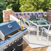 A view of an elevated patio with a dining room set, grill and American flag embordered railways.